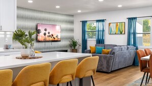 Uma sala de estar moderna com um sofá cinzento, poltronas amarelas e uma televisão na parede.