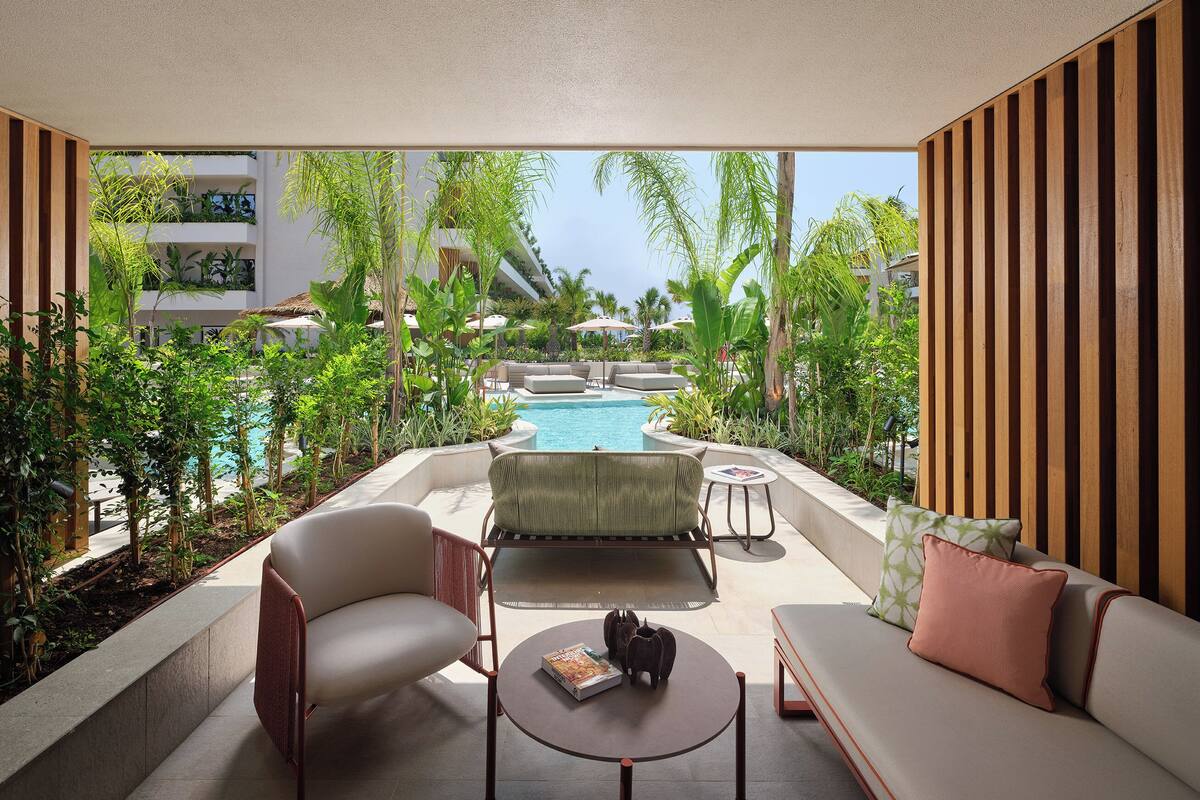 A modern outdoor seating area with a pool, surrounded by lush greenery and a clear view of the ocean.