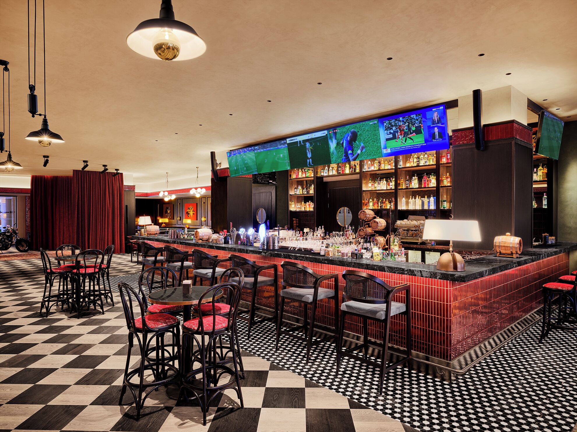 A bar area with a checkered floor, bar stools, and a television screen displaying a sports event.