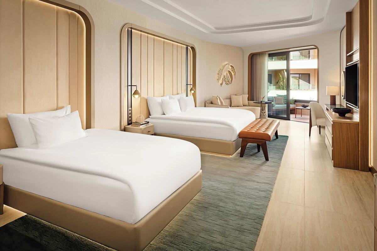 A hotel room with two beds, a desk, a chair, a TV, and a large window.