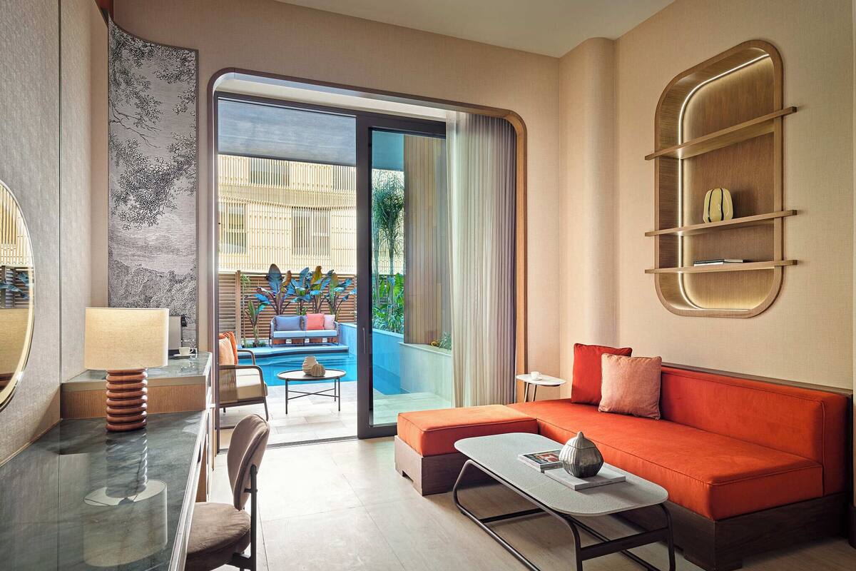 A modern hotel room with a glass dining table, a sofa, a small coffee table, and a pool view.