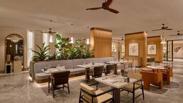 Restaurante moderno com pé-direito alto, ventiladores no teto e diversas opções de assentos, incluindo cabines e mesas.