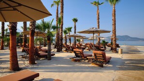 A beachside lounge area with sun loungers and palm trees, overlooking a clear blue sea. - XO Cape Arnna Fethiye (Fethiye)