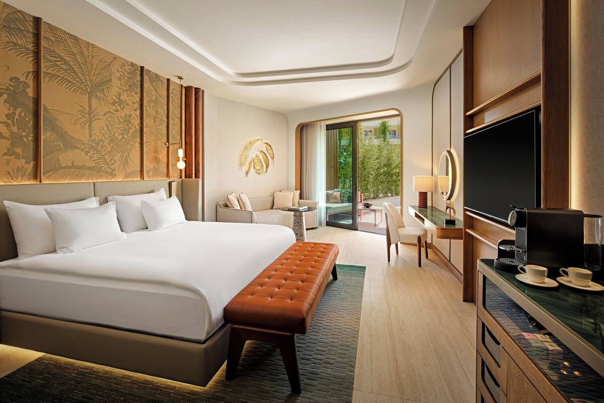 A modern hotel room with a large bed, a seating area with a sofa and chairs, a television, and a coffee machine.