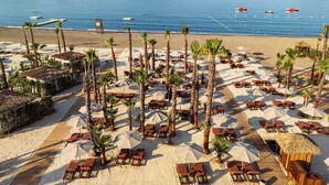 A beach resort with rows of sun loungers and palm trees, a wooden deck, and a view of the sea and mountains. - XO Cape Arnna Fethiye (Fethiye)