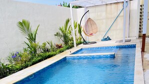 Une piscine rectangulaire à l’eau d’un bleu limpide, entourée d’une terrasse carrelée et agrémentée de diverses plantes.