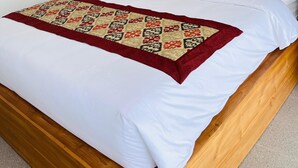 Un lit bien fait, avec du linge de lit blanc, un plaid à motifs rouges et beiges, et trois éléments décoratifs accrochés au mur au-dessus.