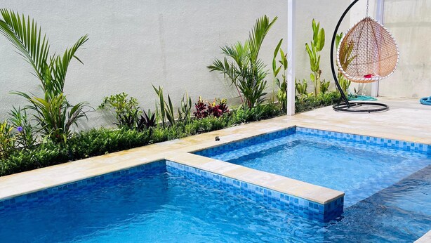 Une piscine rectangulaire à l’eau d’un bleu limpide, entourée d’une terrasse carrelée et agrémentée de diverses plantes.