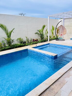 Ein rechteckiger Pool mit klarem, blauem Wasser, umgeben von einer gefliesten Liegefläche und verschiedenen Pflanzen.