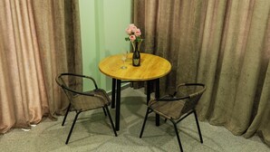 A round wooden table with two wicker chairs, a vase with pink flowers, and a wine bottle. - Panorama David Apart-Hotel (T'bilisi)