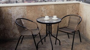 A balcony with two wicker chairs and a small round table, overlooking a cityscape. - Panorama David Apart-Hotel (T'bilisi)
