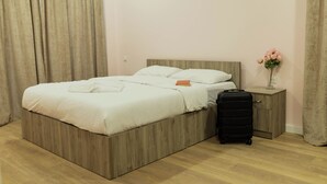 A neatly made bed with a wooden headboard, a small bedside table with a vase of flowers, and a suitcase on the floor. - Panorama David Apart-Hotel (T'bilisi)
