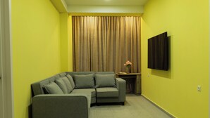 A room with a sectional sofa, a flat-screen TV mounted on the wall, and a curtain covering a window. - Panorama David Apart-Hotel (T'bilisi)