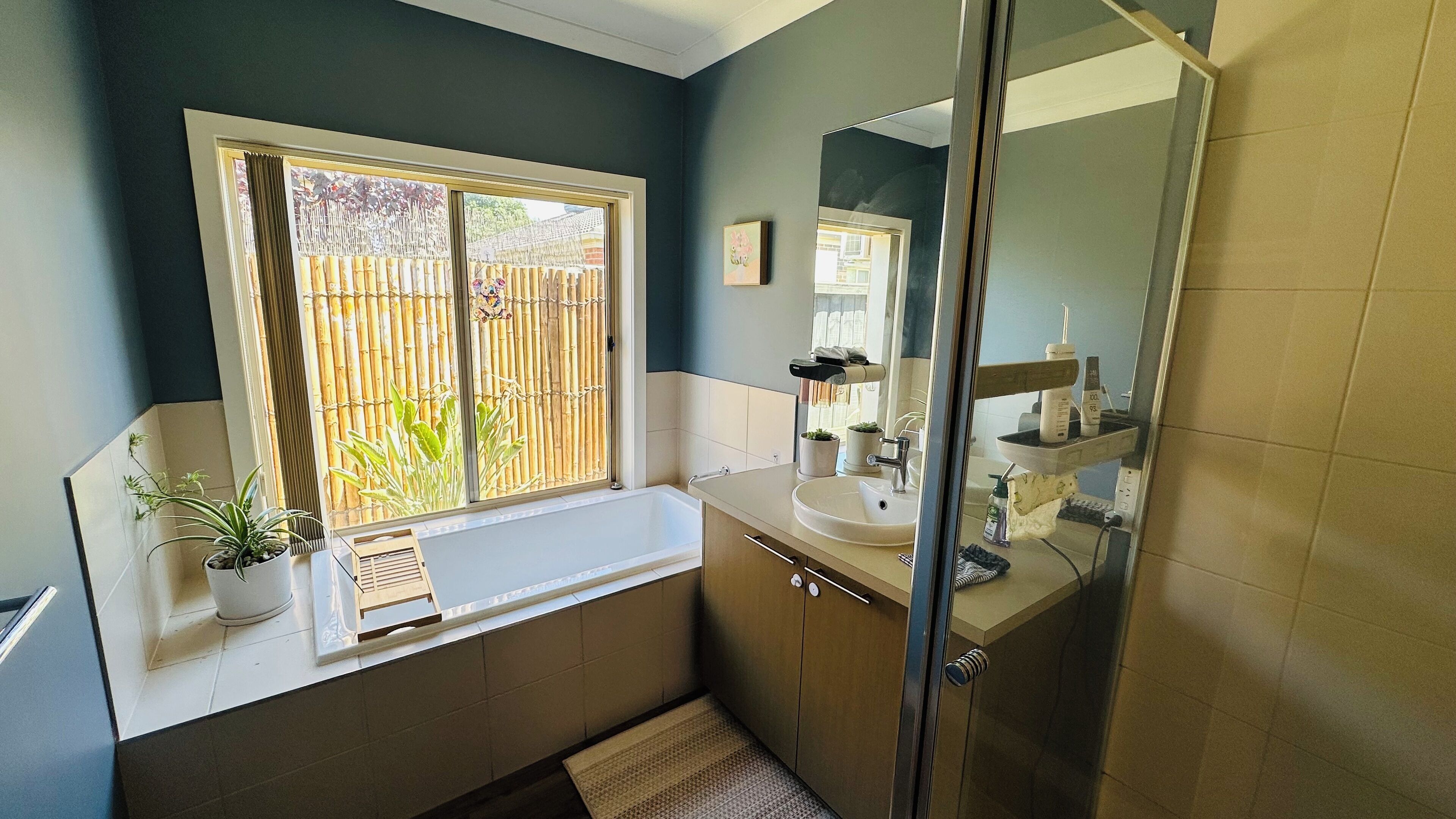 Bagno con vasca, lavabo e cabina doccia. Si vede una finestra con vista su una staccionata di bambù e vegetazione.