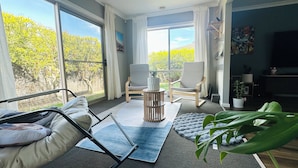 Amplia sala de estar con ventanas grandes, ventilador de techo y vistas al exterior.