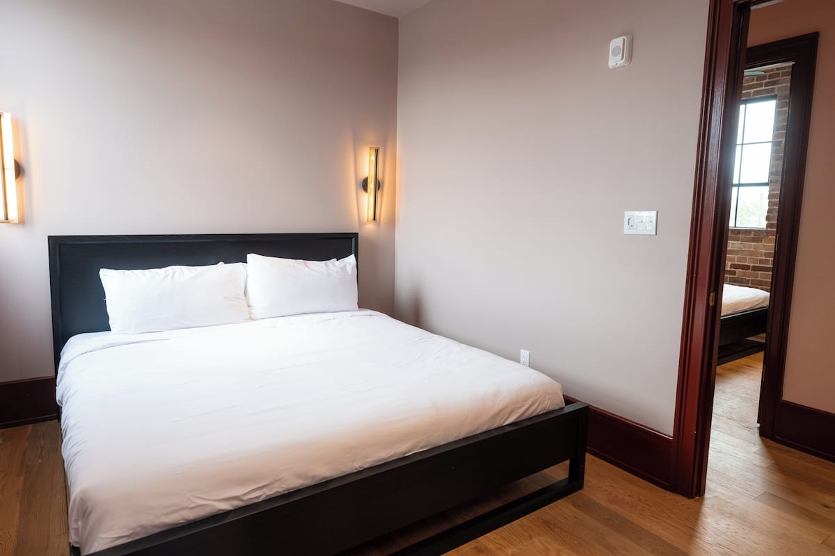 A neatly made bed in a room with a wooden floor and a brick wall.