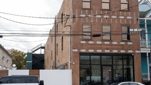 A multi-story brick building with a large glass storefront, multiple windows, and visible electrical wires. - Gisele Hotel (New Orleans)
