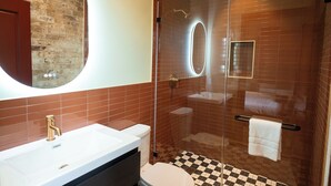 A modern bathroom with a white sink, a round mirror, a glass-enclosed shower, and a checkered floor. - Gisele Hotel (New Orleans)