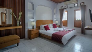 A hotel room with a wooden headboard, a bed with white and red bedding, a bench, a nightstand with a lamp, and a mirror.