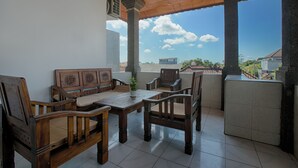 A covered outdoor seating area with a wooden table and chairs, a potted plant, and a view of the cityscape.