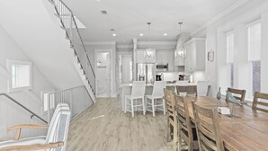 A spacious kitchen with white cabinetry, a wooden dining table, and a staircase leading to an upper level.