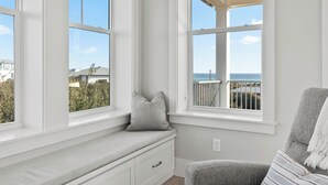 A room with a built-in bench by a large window overlooking a balcony with a view of the sea.