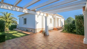 Un patio cubierto con piso de baldosas, columnas blancas y un edificio blanco con techo de tejas.