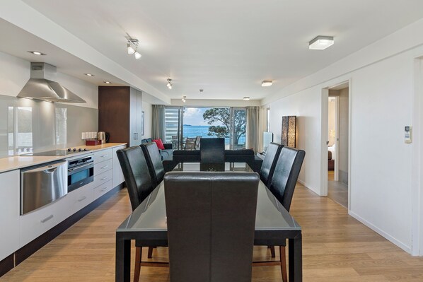 A modern kitchen with a dining area, large windows, and a view of the sea.