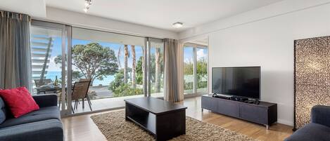 A modern living room with a large TV, dark sofas, a coffee table, and a view of the outdoors.