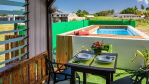 Een overdekt buitengebied met een zwembad, een eettafel gedekt met borden en glazen, en uitzicht op een woongebied met huizen en groen.