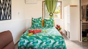 Een slaapkamer met een bed, een raam met groene gordijnen, een witte airconditioning en een bruine stoel.