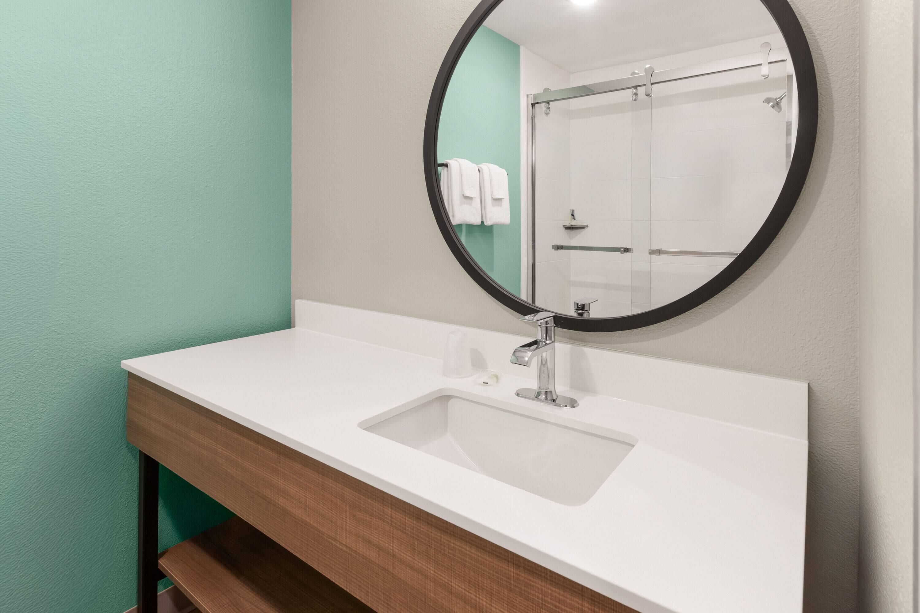 A bathroom with a white sink, a round mirror, and a green wall.