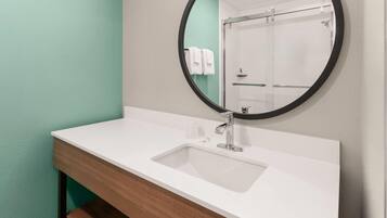 Un baño con un lavabo blanco, un espejo redondo y una pared verde.
