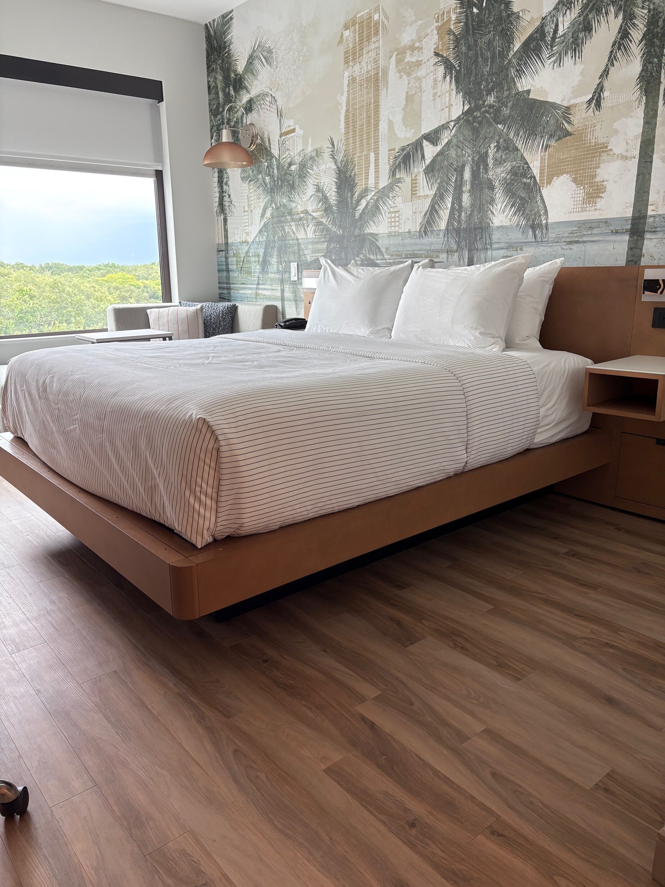 A modern bedroom with a large bed, wooden flooring, and a cityscape mural on the wall.