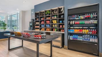 Un moderno vestíbulo de hotel con mostrador de recepción, estantes de aperitivos y refrigerador para bebidas.