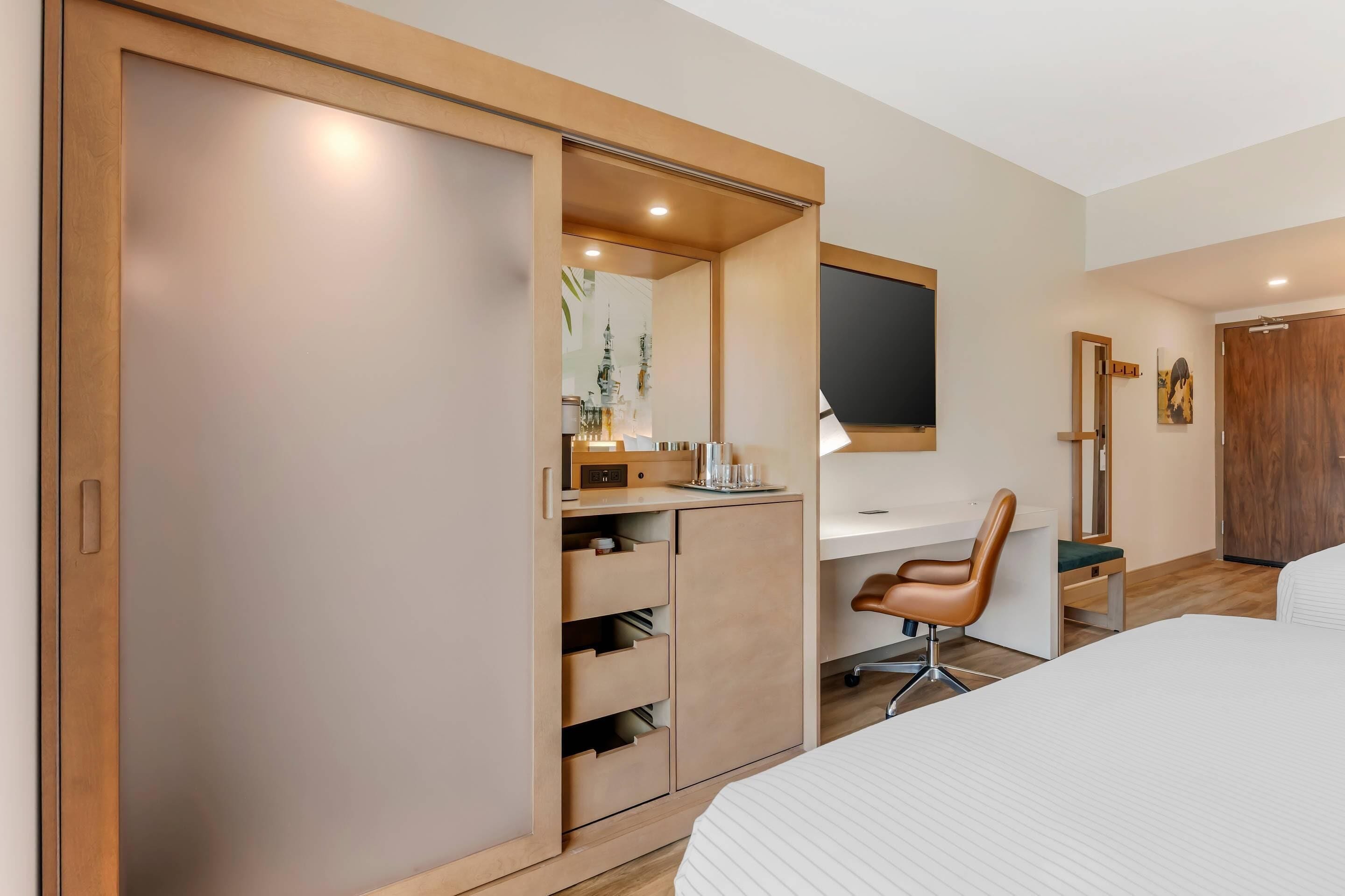 Una camera d'albergo moderna con un letto grande, una scrivania con una sedia, un armadio e un televisore.