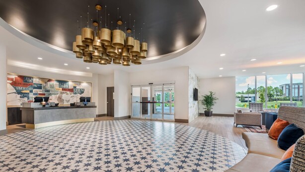 A spacious lobby with a patterned floor, a reception desk, and seating area with a view of the outdoors. - Cambria Hotel Tampa-Brandon (Tampa)