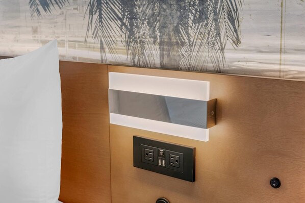 Una habitación moderna con pared de paneles de madera, almohada blanca y estación de carga integrada con dos puertos USB y toma de corriente.