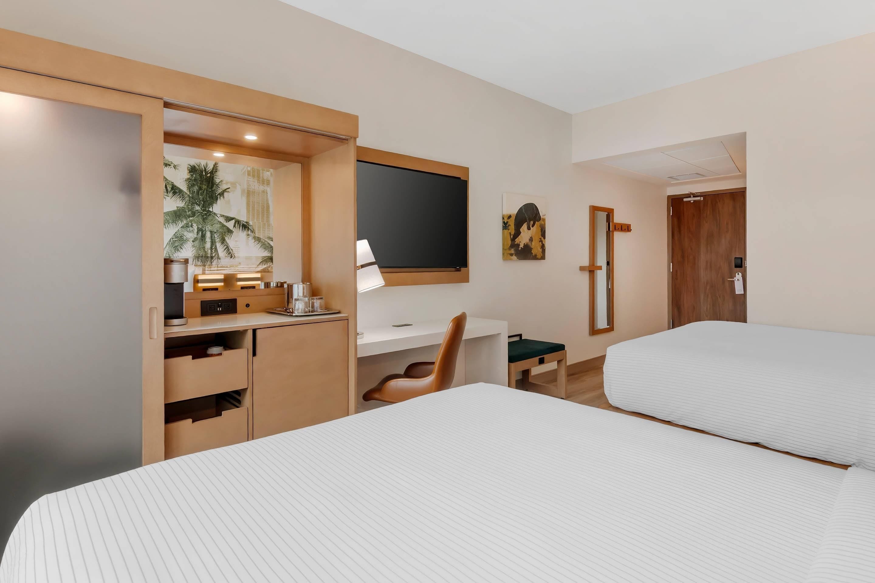 Ein Hotelzimmer mit Bett, Schreibtisch mit Computer, Stuhl, Fernseher und einer Tür.