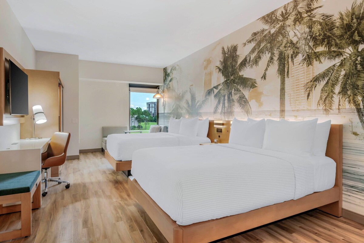 Een hotelkamer met twee bedden, een bureau, een stoel en een groot raam.