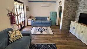 A living room with a blue sofa, a wooden coffee table with a compass rug, a teal refrigerator, and a TV on a wooden cabinet.