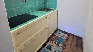 A compact kitchen with teal tiles, a sink, and cabinets. There's a decorative rug with nautical themes and a wall decal of a beach scene.