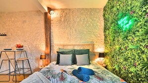 A bedroom with a bed, a nightstand, a lamp, a small table with chairs, and a green wall with a neon sign. - ღ Jungle Rochelaise • Hypercentre, 4K TV, Fibre (La Rochelle)