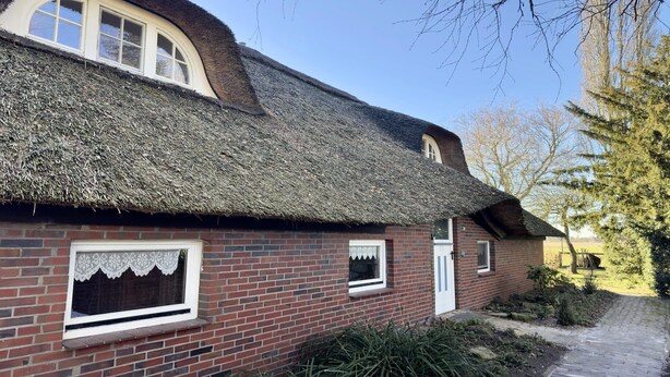 A traditional brick house with a thatched roof and a small garden. - Ferienwohnung im Reetdachhaus, Burhave (Burhave)