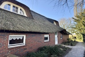 Et traditionelt murstenshus med stråtækt tag og en lille have.