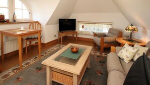 A cozy loft-style living space with a dining area, a sofa, a television, and a lamp. - Ferienwohnung im Reetdachhaus, Burhave (Burhave)