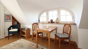 A cozy attic room with a wooden table and chairs, a bookshelf, and a window with a view. - Ferienwohnung im Reetdachhaus, Burhave (Burhave)