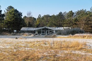 Ein Gebäude mit Satteldach, umgeben von einem Feld und Bäumen.