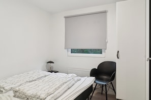 Ein Schlafzimmer mit Bett, Stuhl, Fenster mit Jalousie und Heizkörper.
