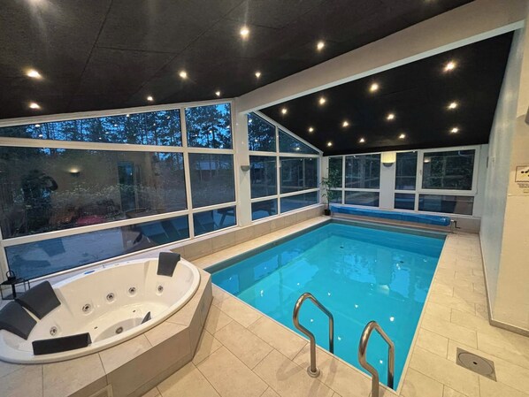 An indoor swimming pool with a hot tub, large windows, and a tiled floor.